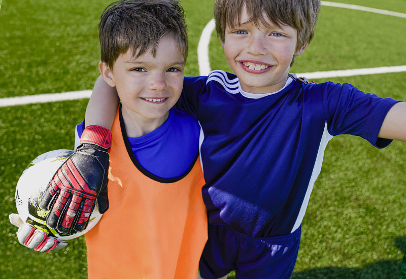 2 unga glada pojkar som håller i fotboll på en fotbollsplan